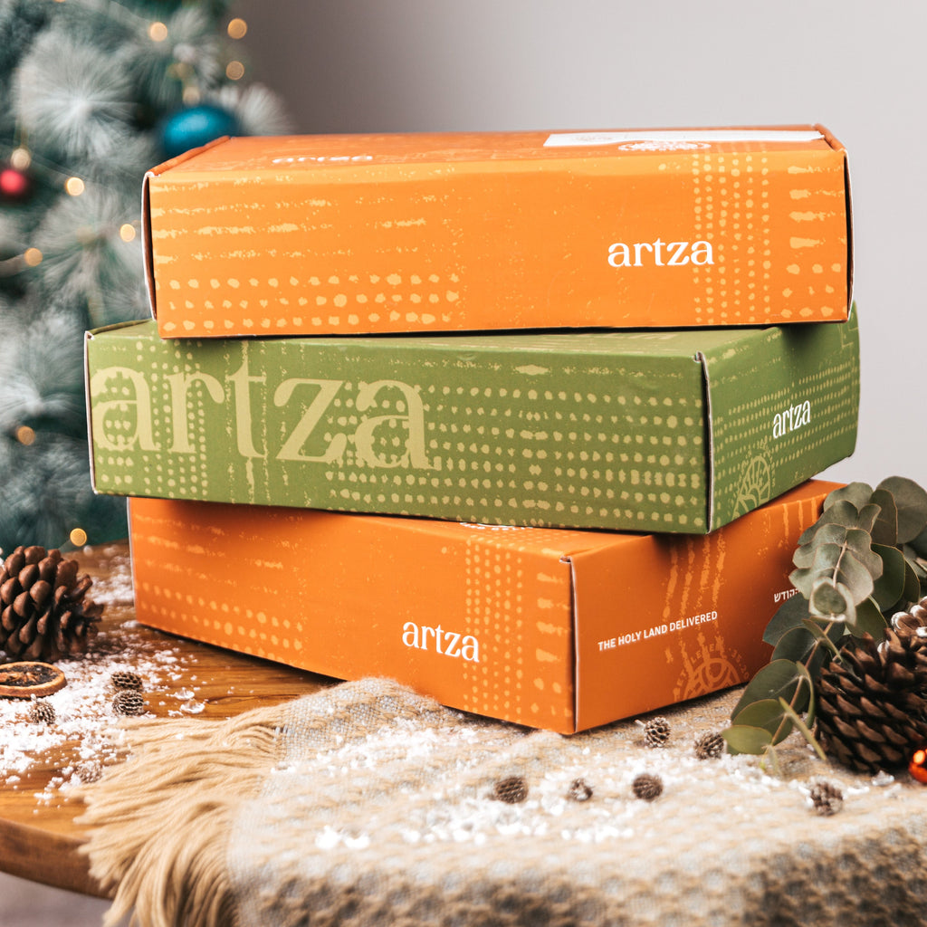 Stack of Artza boxes on a wooden surface with a Christmas tree in the background