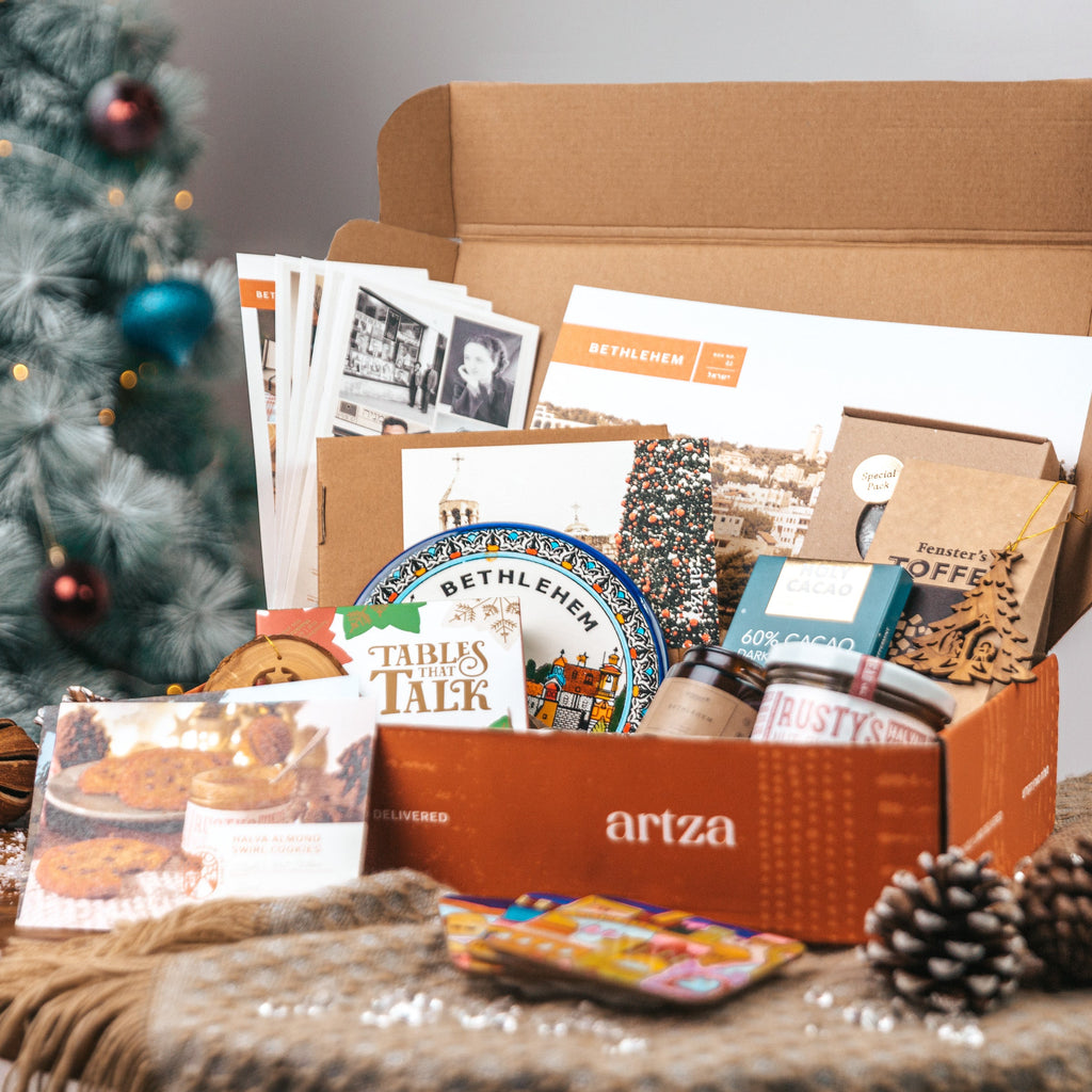 Open box from Arza with holiday-themed items including a Christmas tree in the background.